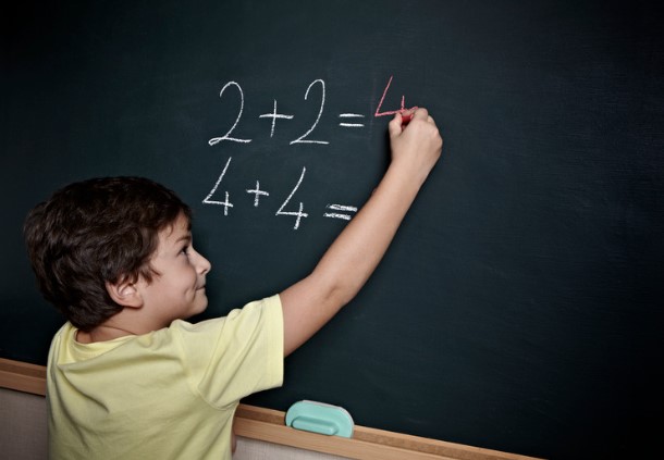 child at chalkboard doing simple addition problems