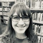 female wearing glasses with books in background,